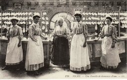 Carte postale ancienne légendée « Vichy — Une famille de donneuses d'eau » : cinq femmes en tablier posent devant la buvette