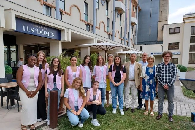 L'équipe de la compagnie, gilets vichy roses, réunie devant la brasserie Les Dômes près des thermes